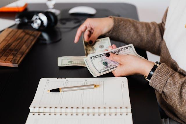 a person counting cash next to an open planner